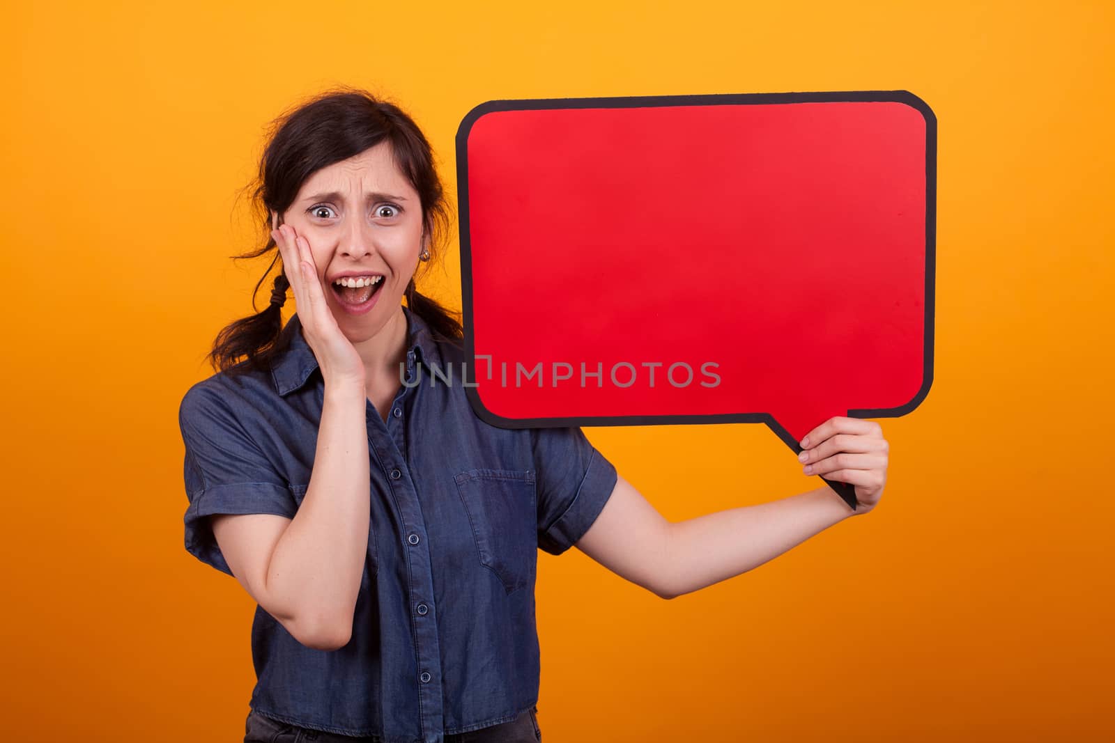 Gorgeous young woman shocked standing with speech bubble in studio over yellow background. Pretty woman with empty placard. Copy space available.