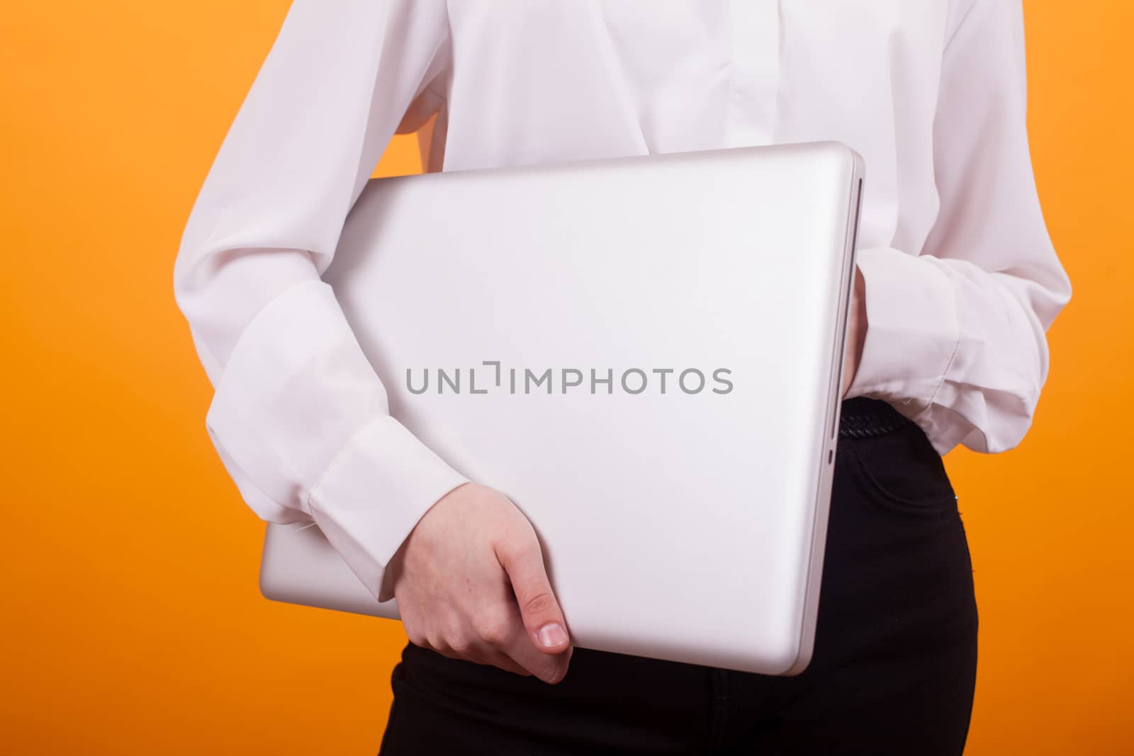 Portrait of young girl holding a laptop in studio over yellow background. Teen girl holding a laptop.