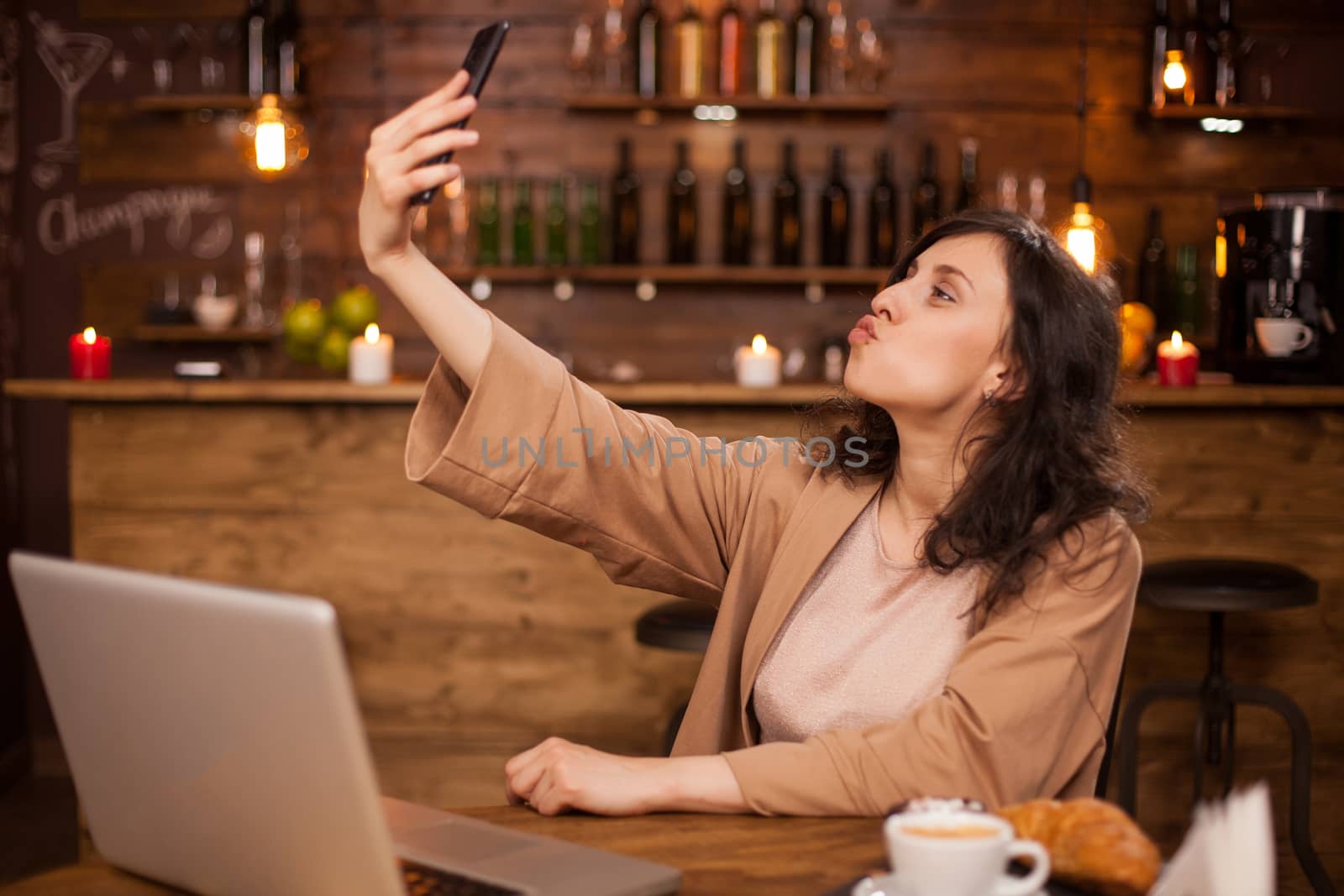 Portrait of attractive young caucasian girl taking selfie in a casual coffee shop. Girl with modern notebook near her in a autehnic coffee shop.