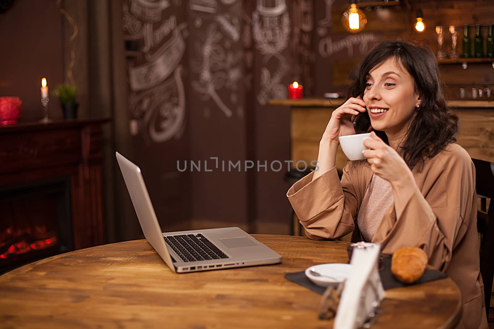 Portrait of caucasian young business woman with compur in a coffee shop. Young female holding coffee cup. Young freelancer talking on smartphone
