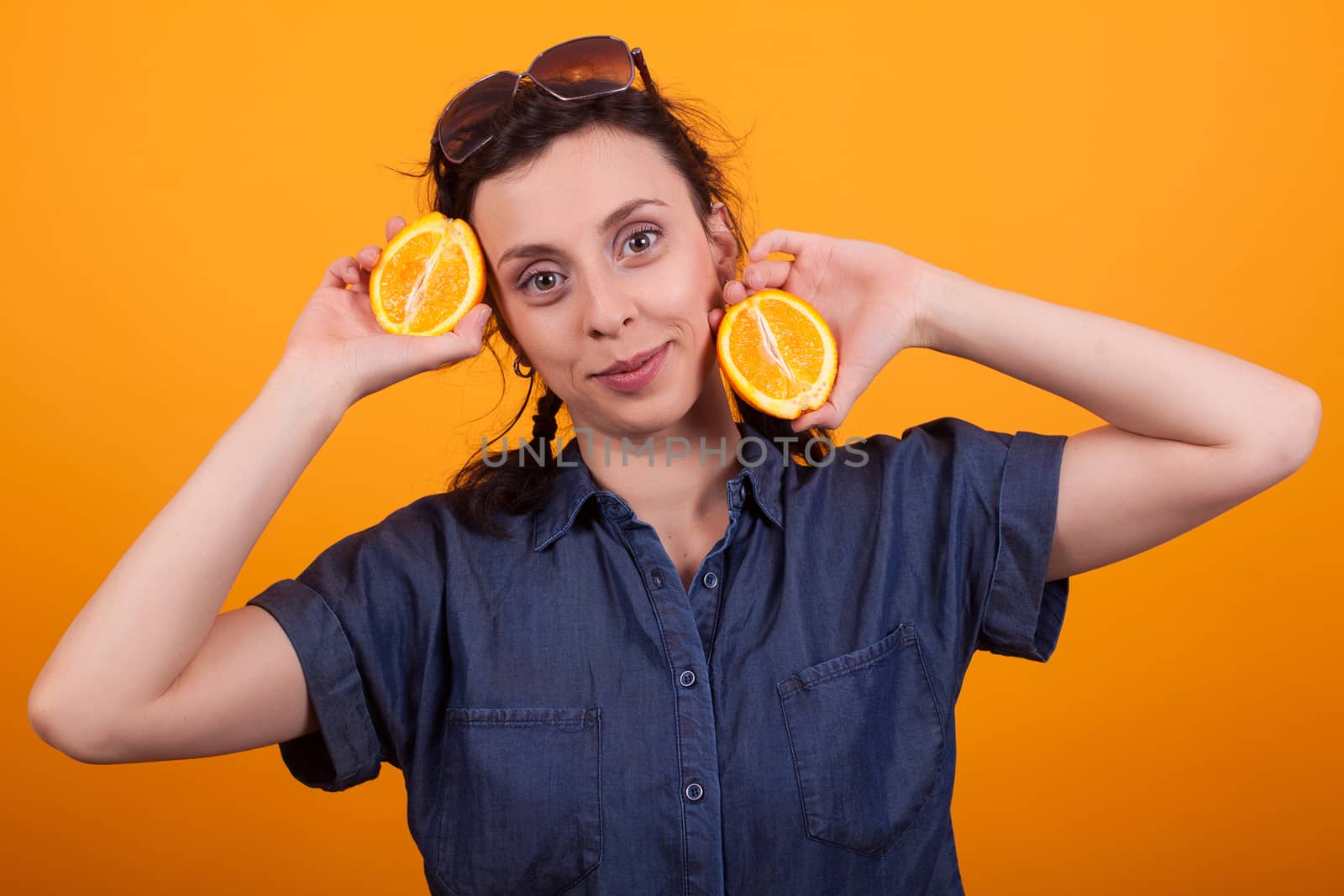 Caucasian pretty girl holding a sliced orange and looking at the camera over yellow background. Joyful girl with juicy oranges.