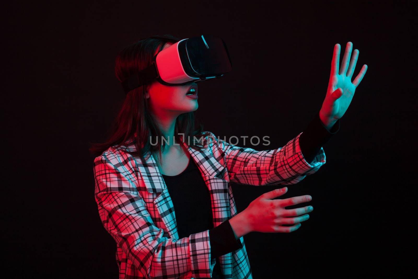 Young girl wearing virtual reality goggles headset in studio with colorful lighting. Futuristic virtual reality goggles.