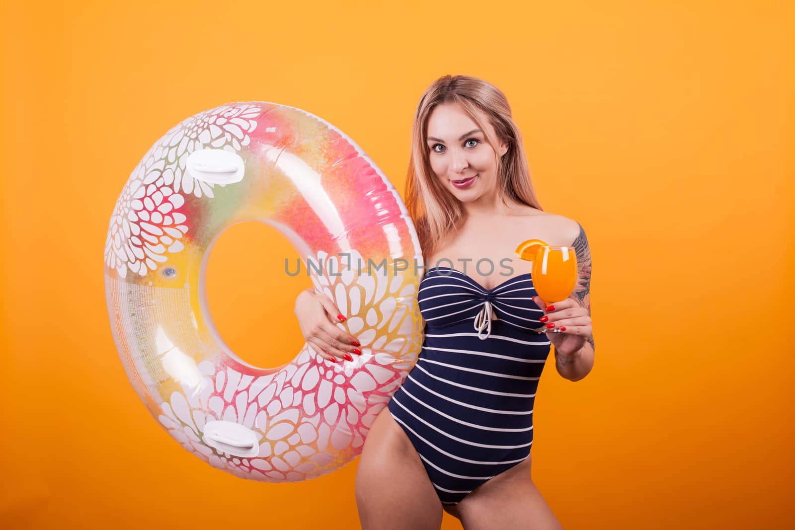 Happy young woman in swimming suit holding summer cocktail over yellow background. Holding swim ring. Attractive woman. Cheerful woman.