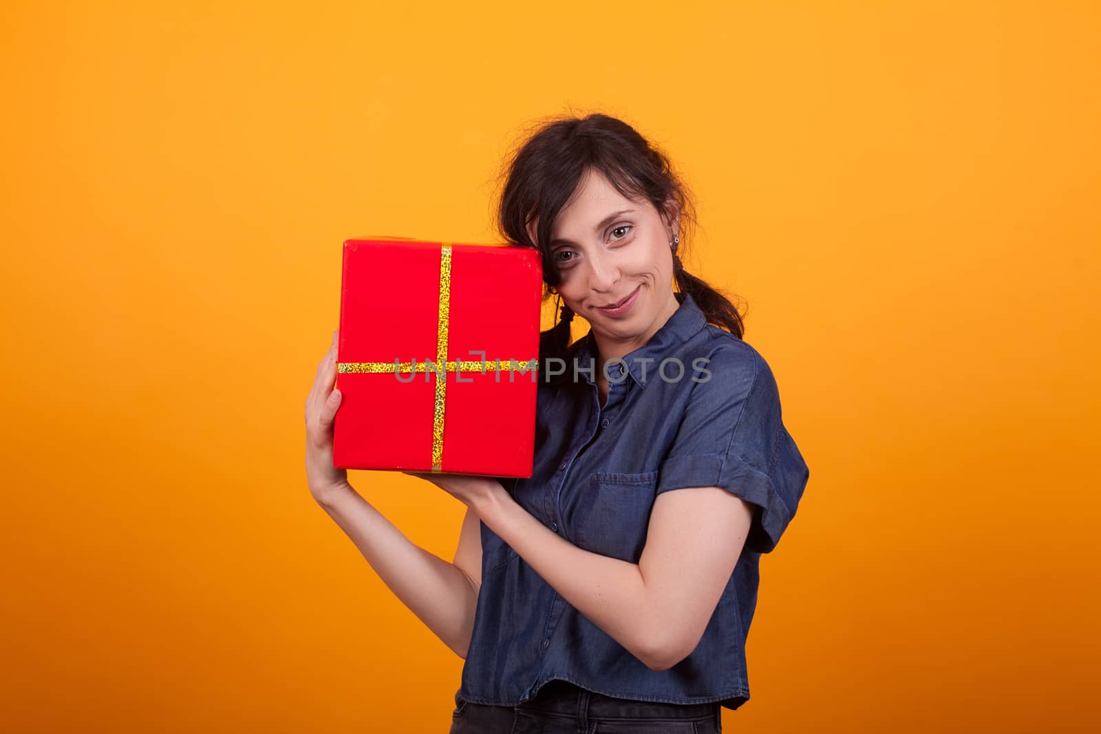 Portrait of happy young woman with her red gift box looking at the camera in studio over yellow background. Cute young woman with gift box. Red gift box.