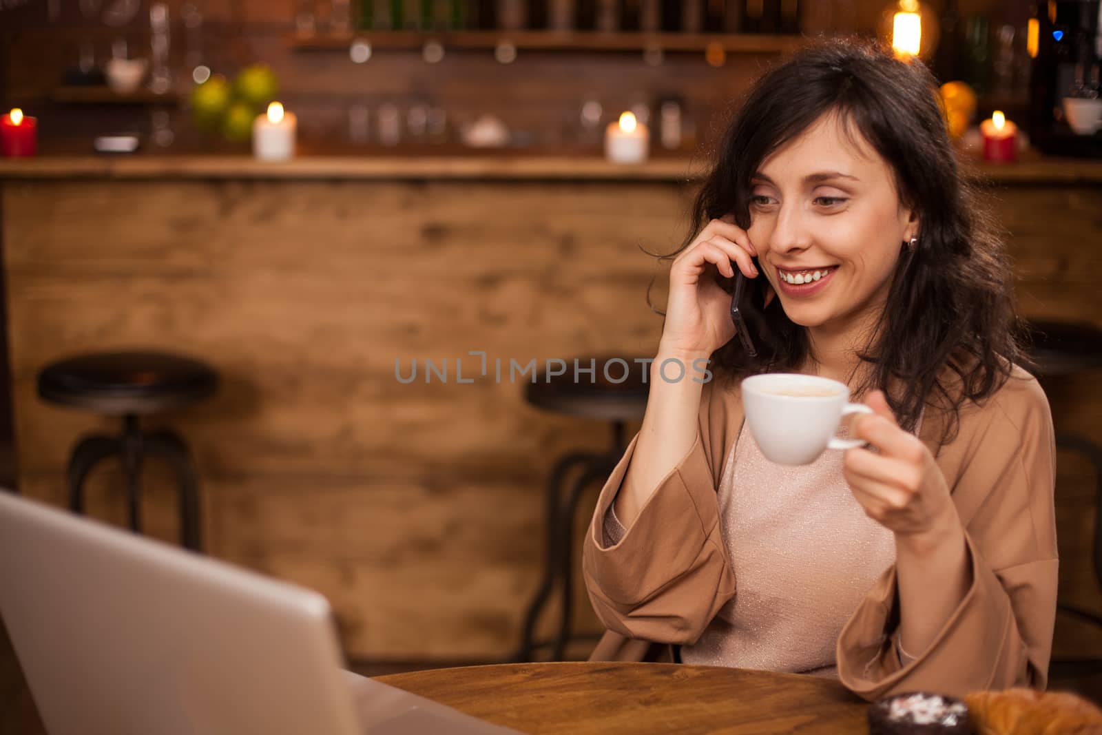Cheerful business woman smilng and looking at her laptop in a coffee shop. Girl with portable computer in a coffee shop. Young freelancer talking on smartphone.