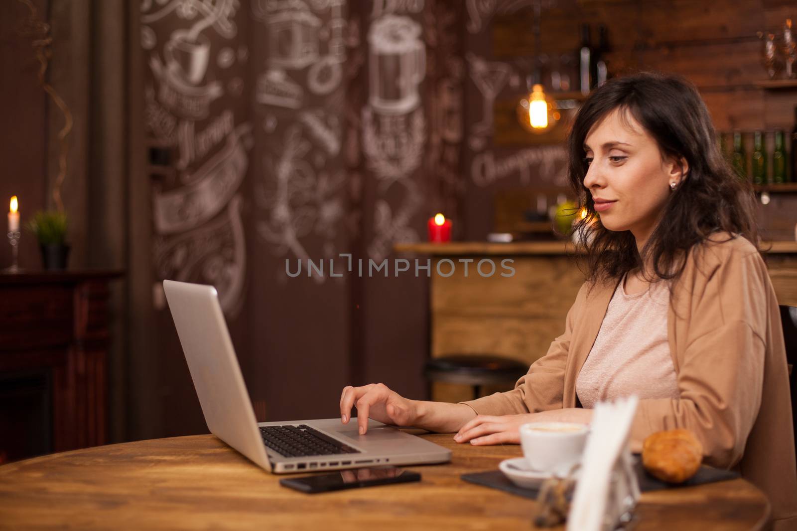 Side view portrait of young female blogger writing her aticle on a coffee shop using her laptop. Young Female entrepreneur doing business on her laptop. Coffee shop with internet connection.