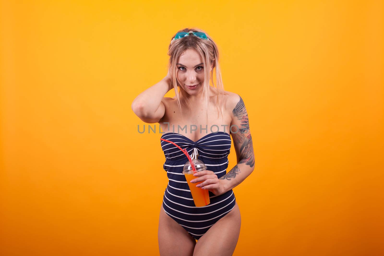 Attractive causian woman with swimming glasses and swimming suit holding glass of delicious orange cocktail. Beautiful young in blue swimming suit.