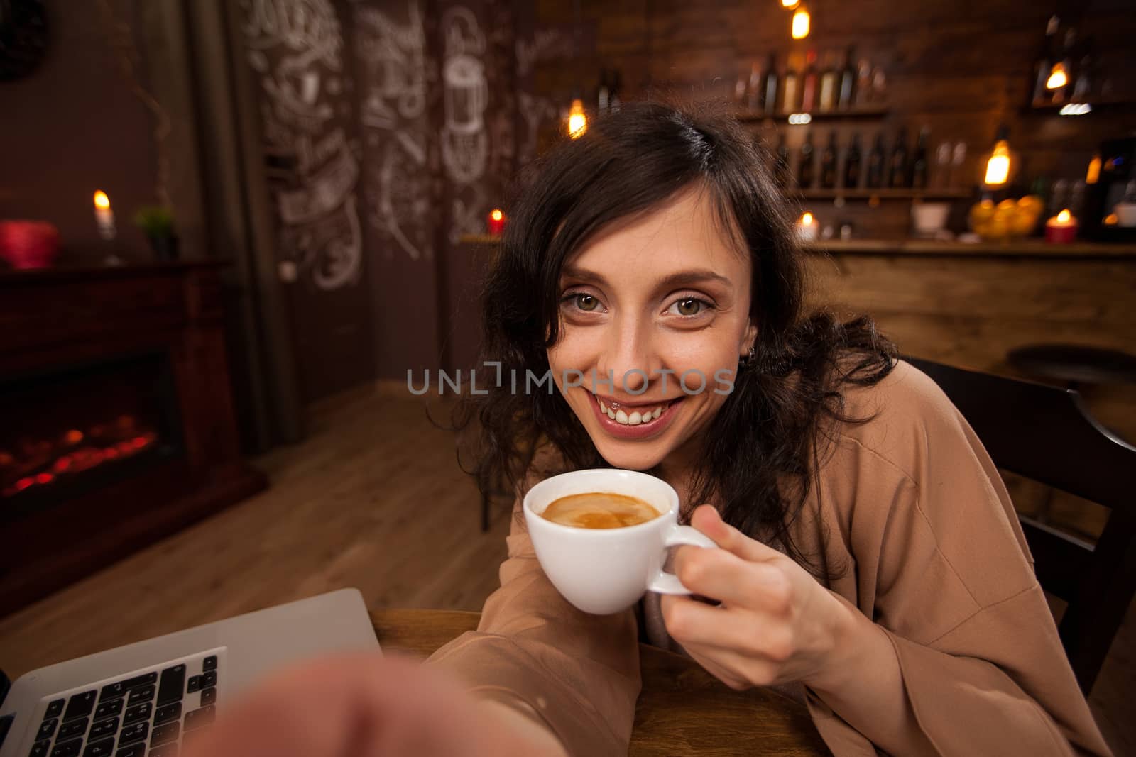 Attractive young woman holding a camera and a cup of coffee taking a selfie. Girl having fun in a coffee shop. Young woman holding a cup of coffee.