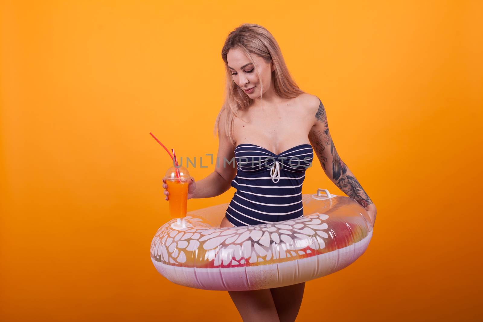 Girl in swimming suit ready for summer vacation over yellow background. Gorgeous young woman with slim body in a swimming ring.
