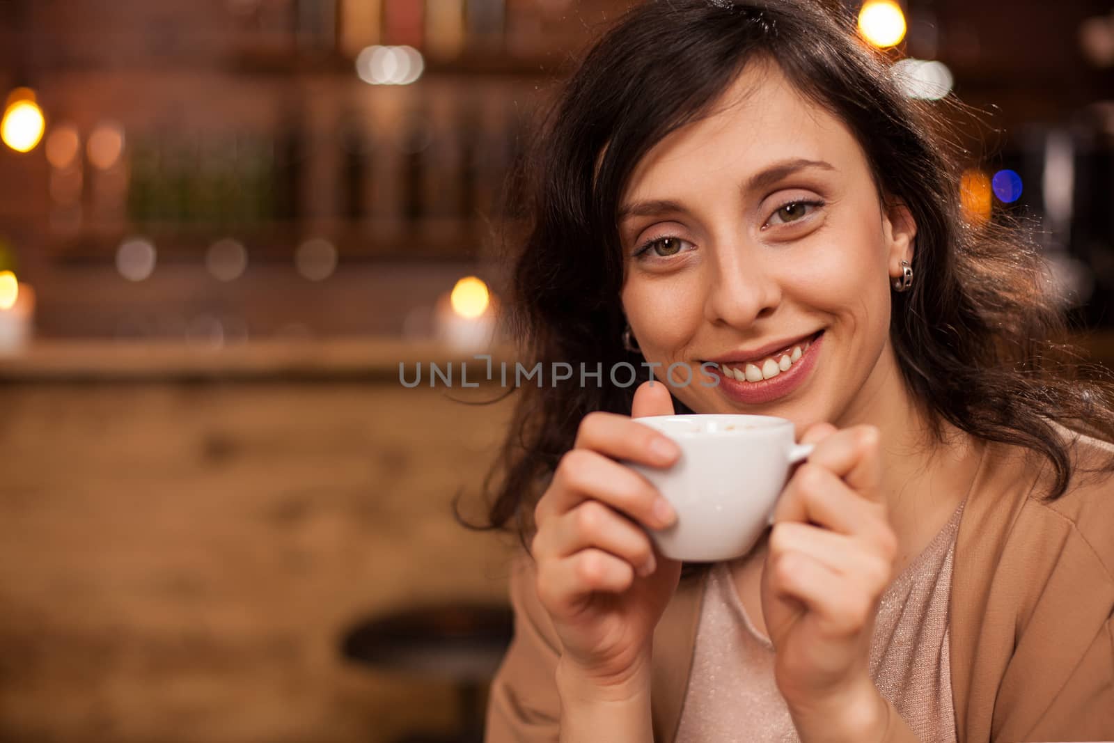 Portrait of beautiful young woman relaxing with a good coffee and smiling at camera in a coffee shop. Attractive woman having an aromatic coffee.