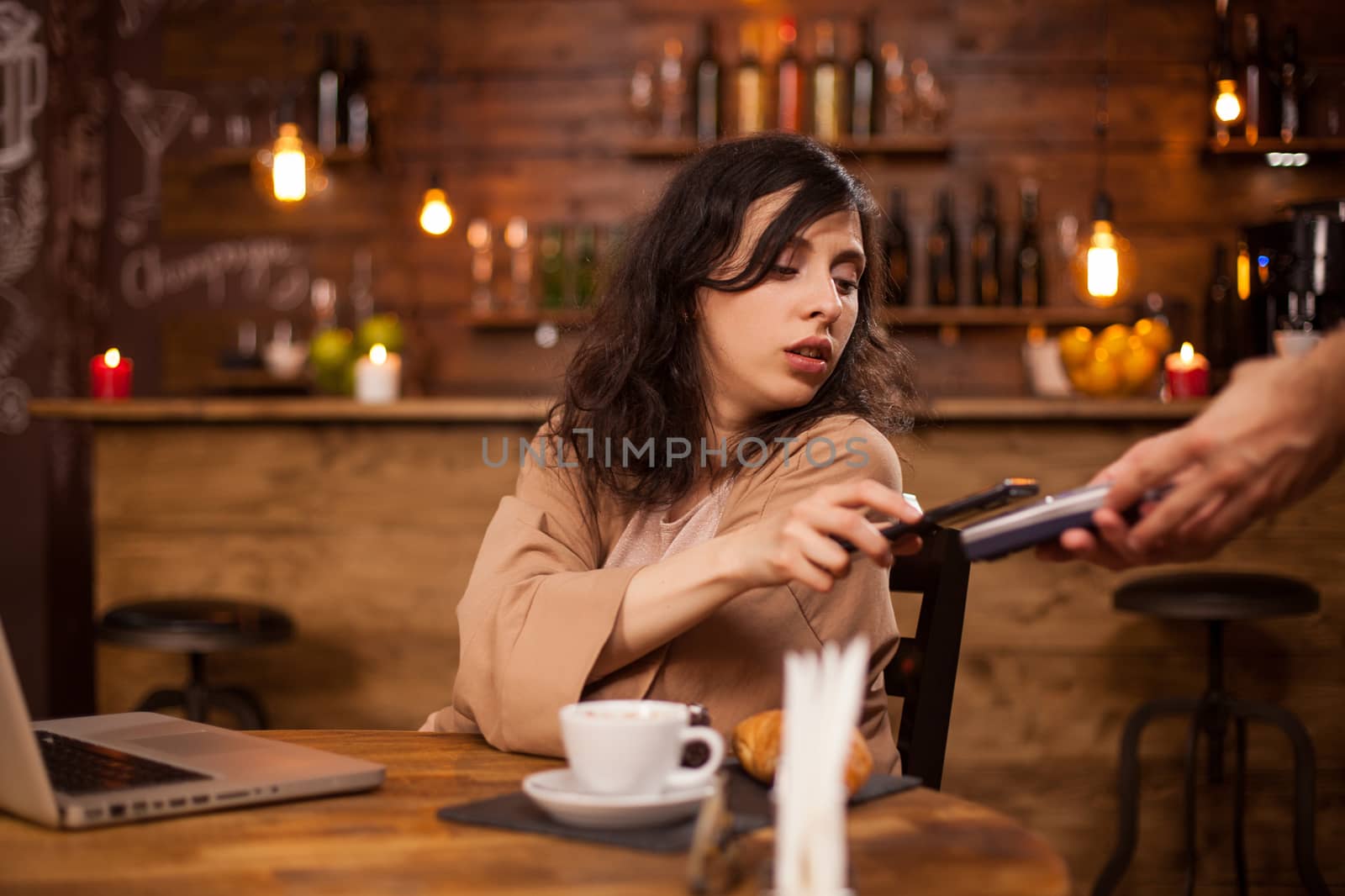Photo of beautiful young woman paying with credit card at a coffee shop. Girl using modern technology to pay for coffee. Paymant technology.