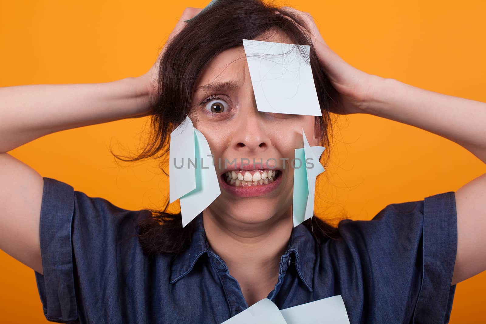 Portrait of beautiful woman frustrated with sticky notes on forehead in studio over yellow background. Girl screaming with reminder notes.
