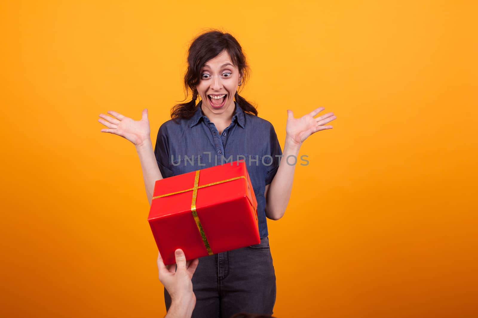 Portrait of amazed beautiful young woman receiving a gift in studio over yellow background. Caucasian beautiful woman shocked.