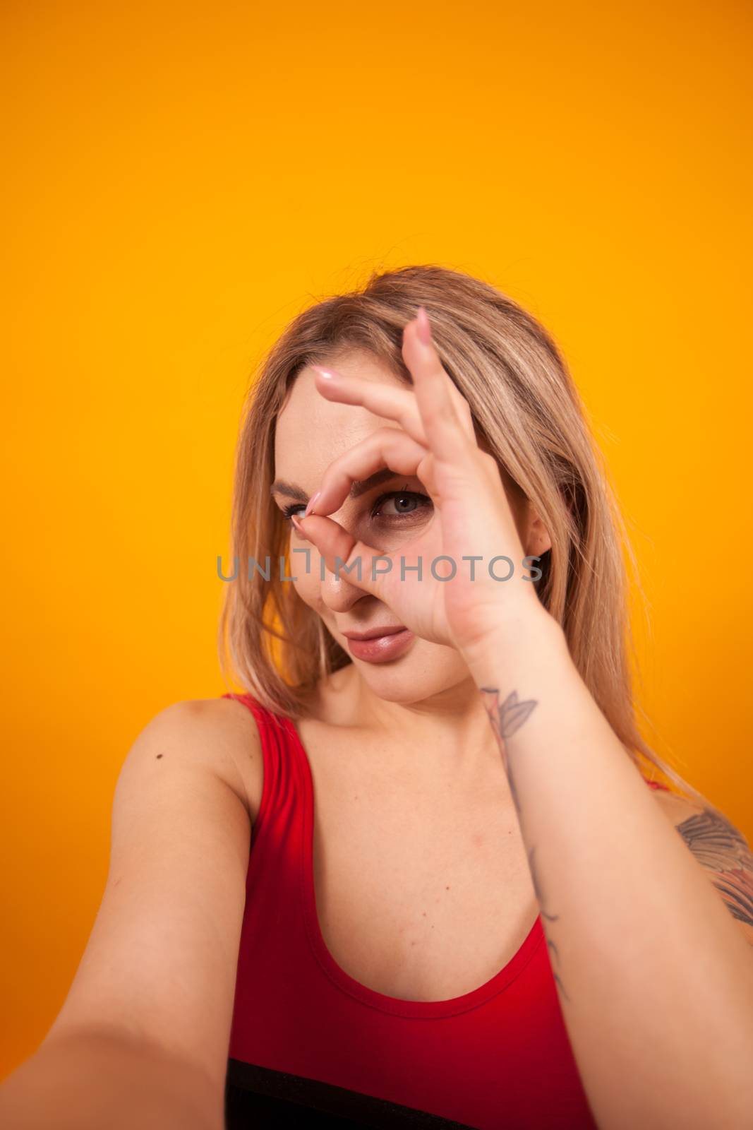 Sexy young woman in red swimming suit making a selfie and showing ok sign over yellow background. Gorgeous young woman in swimming suit.