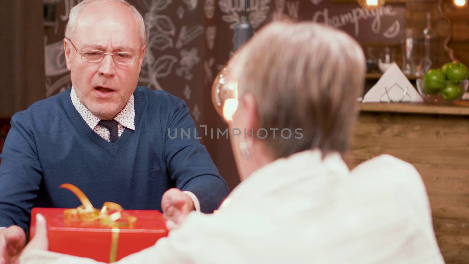 Senior man shocked by the gift that his wife gave him during mealtime in a restaurant. Mature couple.