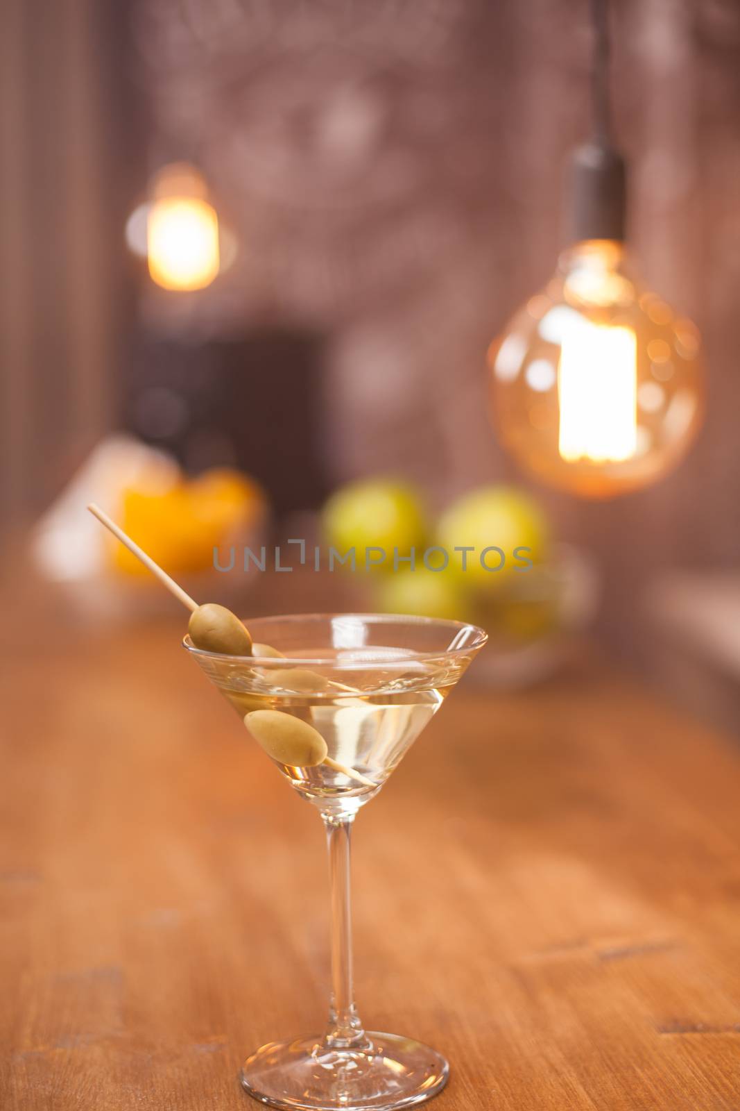 A glass of martini on a bar counter with fruits blured in the background.