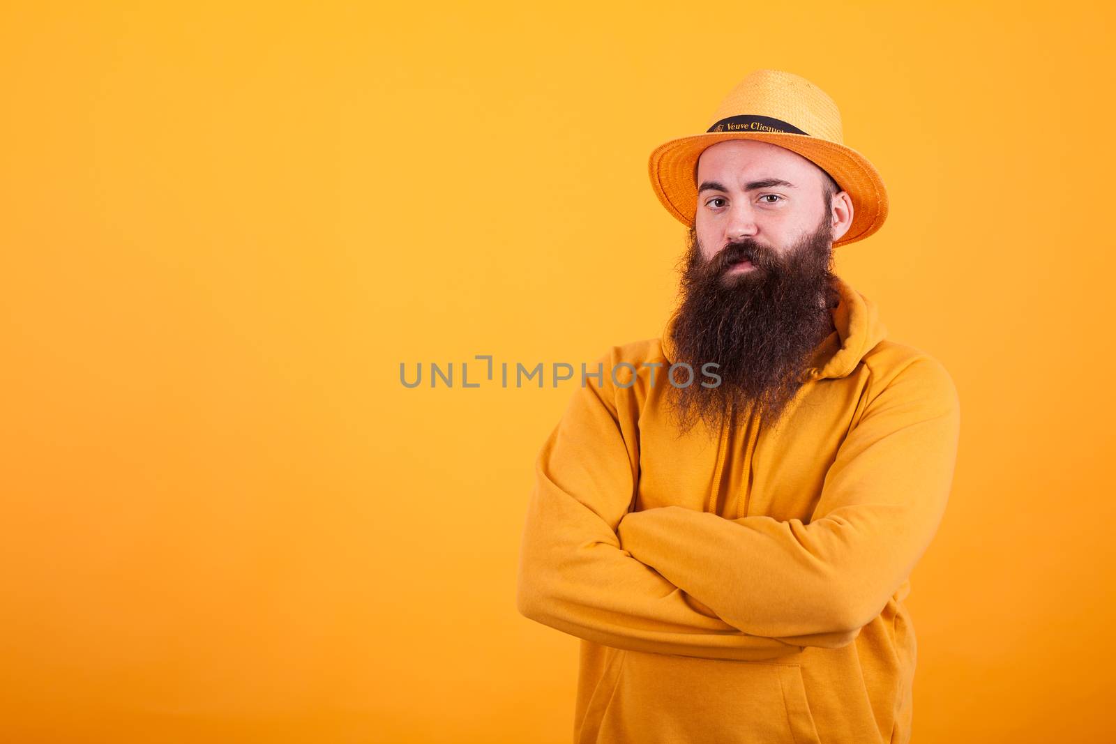 Bearded man with orange hat on his hat holding his arms crossed over yellow background. Confident man. Looking at the camera.