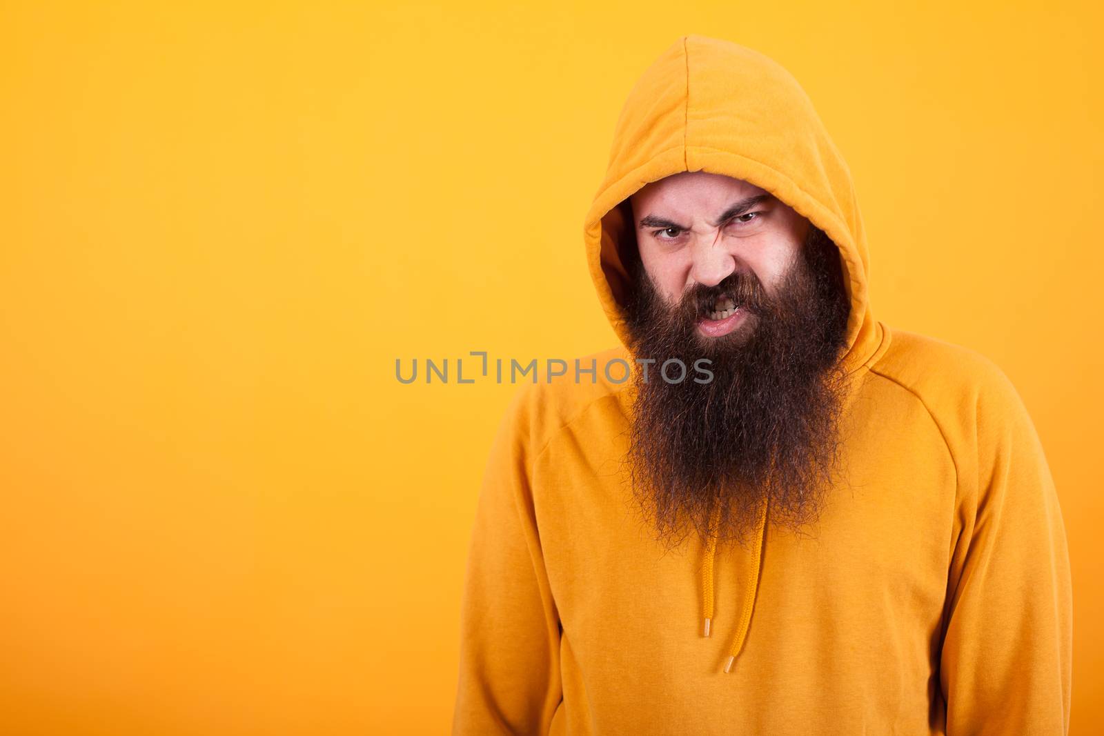 Cool bearded hipster looking at the camera with angry face over yellow background. Trendy man. Stylish man.
