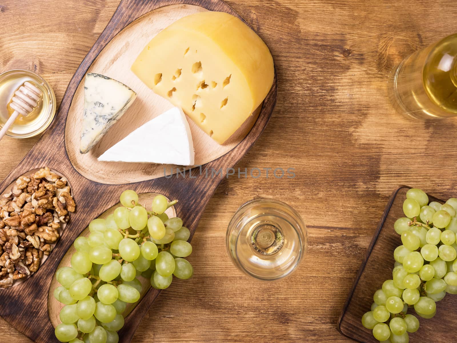 Flat lay top view of various cheeses next to fresh grapes, glass of wine on a wooden table. Copy space available.