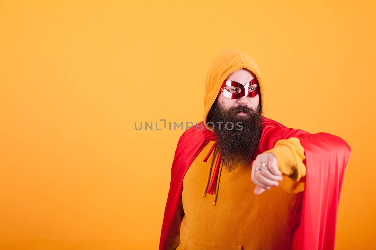 Hipster with long beard dressed in superhero costume looking away over yellow background. Yellow hoodie. red mask. Brave man.
