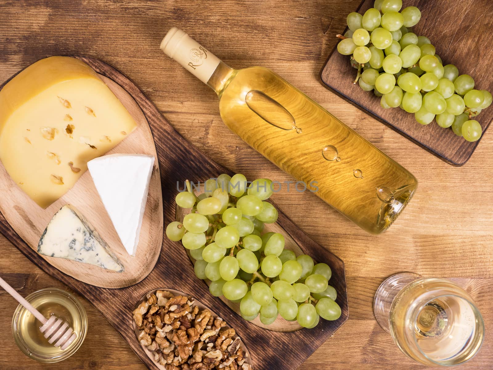 Top view of a bottle of white wine next to fresh grapes on wooden table. Various cheeses. French cuisine.