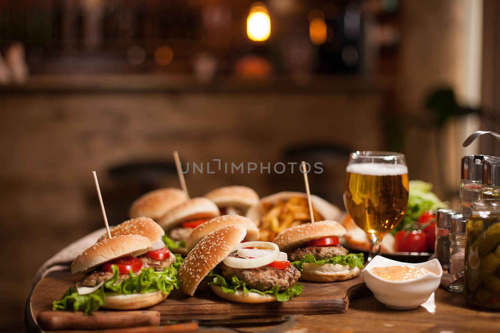 Different mini humbers with wooden spikes and garlic sauce. Golden beer. Blurred counter bar in the background.