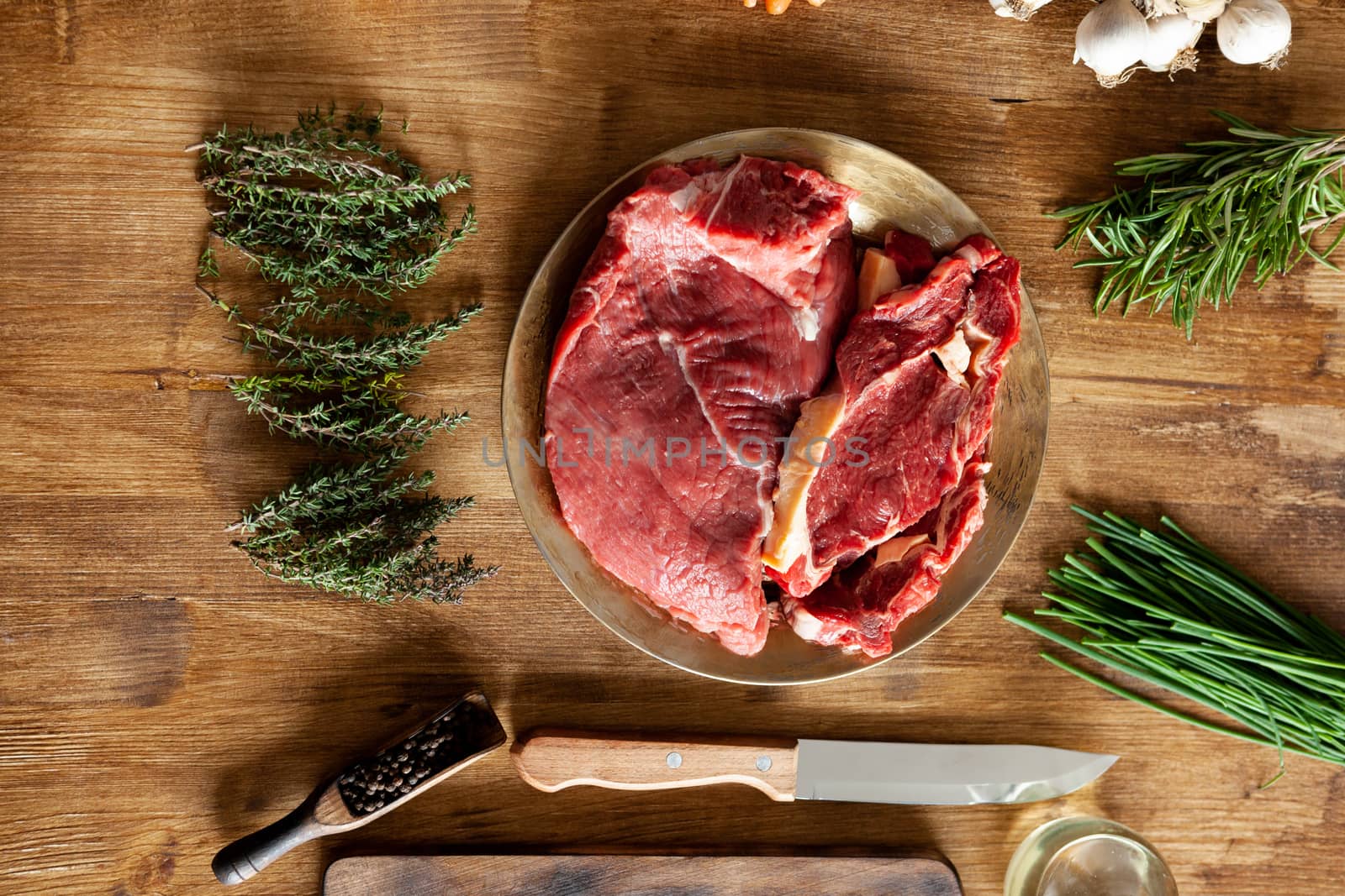 Chunks of red meat next to green herbs on vintage wooden table. Natural protein.