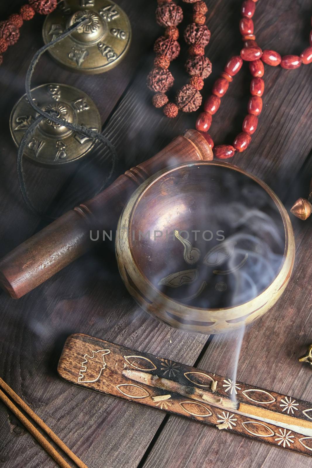copper singing bowl and a wooden stick on a brown table, incense stick burning