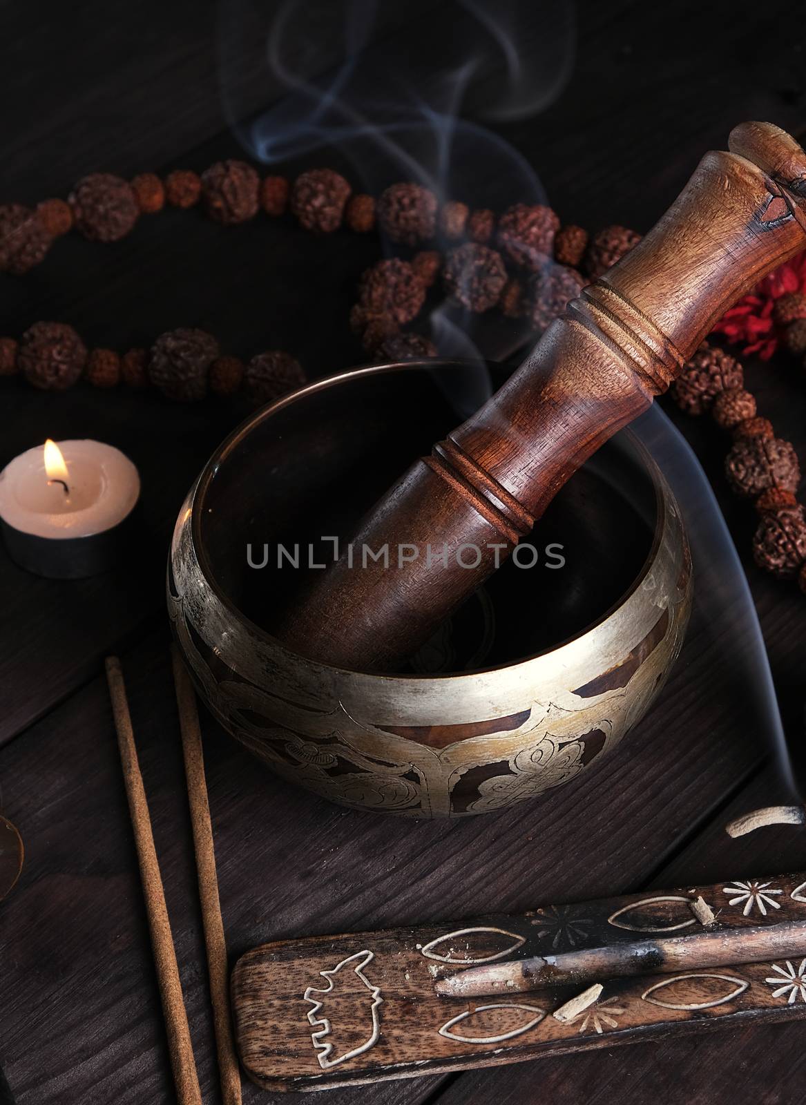 copper singing bowl and a wooden stick on a brown table, a stick with incense is burning nearby