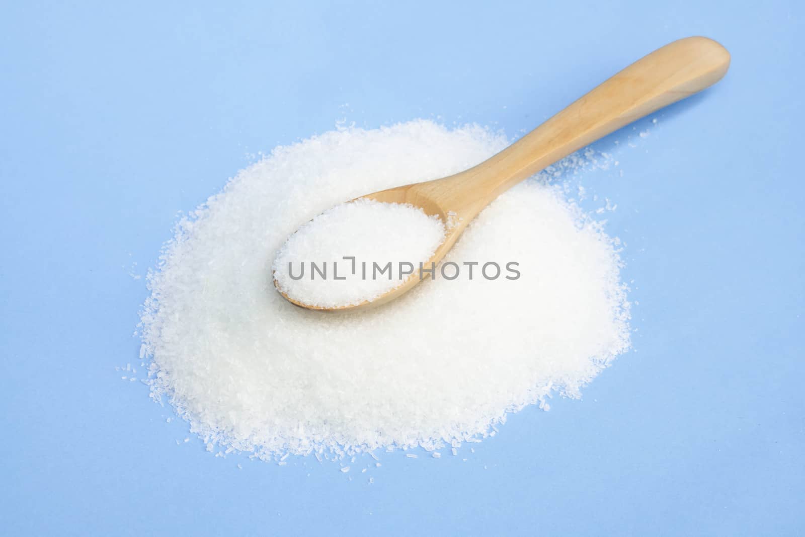 Monosodium glutamate in wood spoon on light blue background, food ingredient