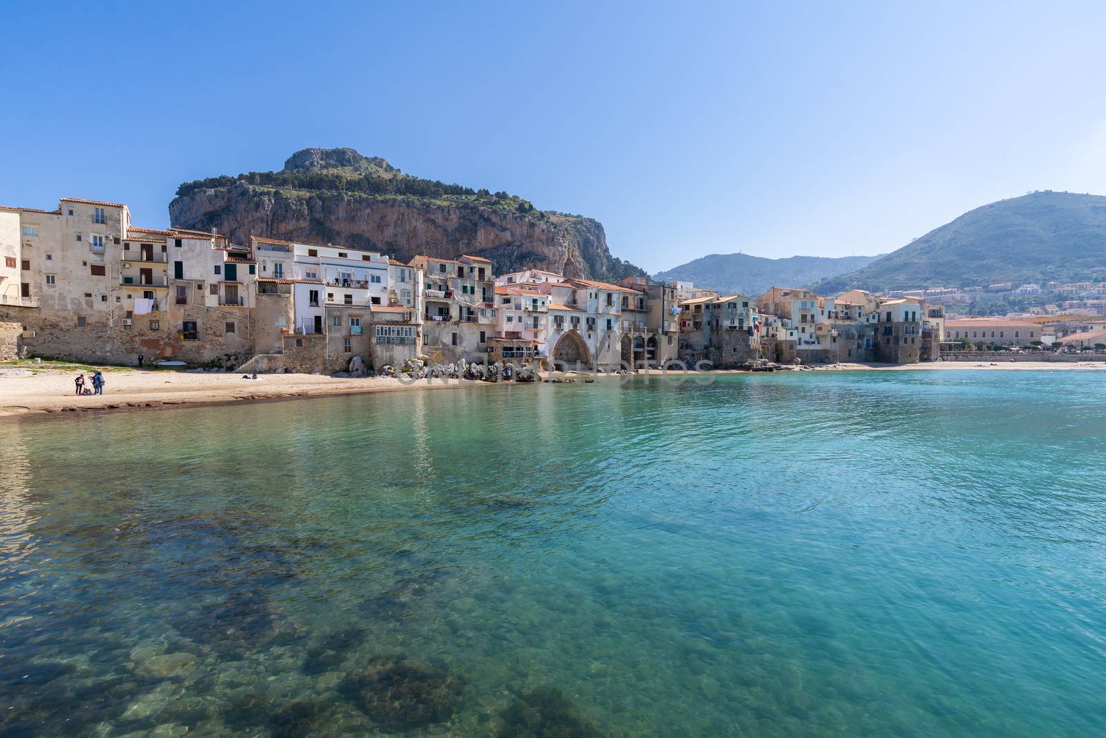 Idyllic view of turquoise sea and houses with Rocca di Cefalu rocky mountain in the background seen from historical old harbour of Cefalu, Sicily, Italy. by tamas_gabor
