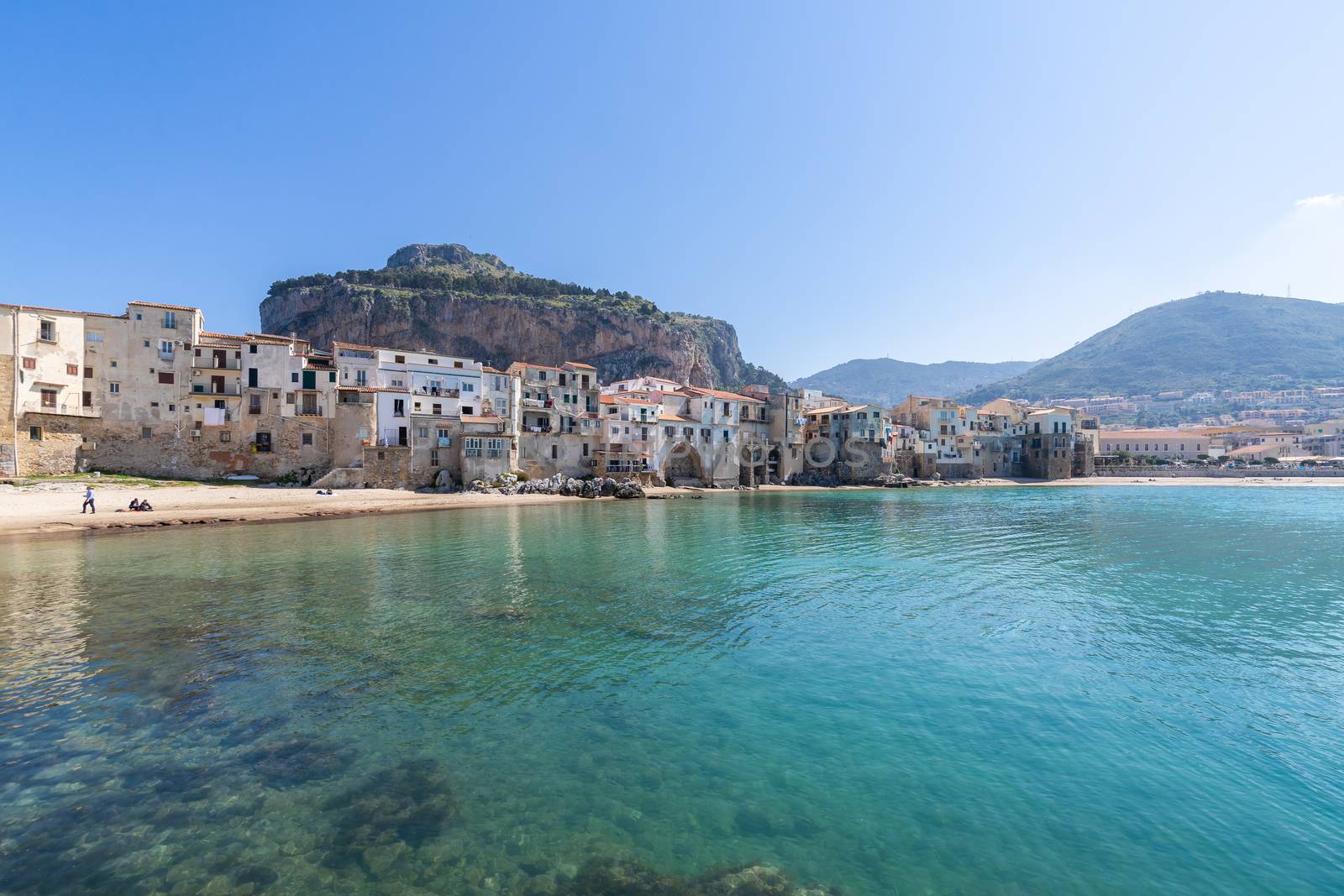 Idyllic view of turquoise sea and houses with Rocca di Cefalu rocky mountain in the background seen from historical old harbour of Cefalu, Sicily, Italy. by tamas_gabor