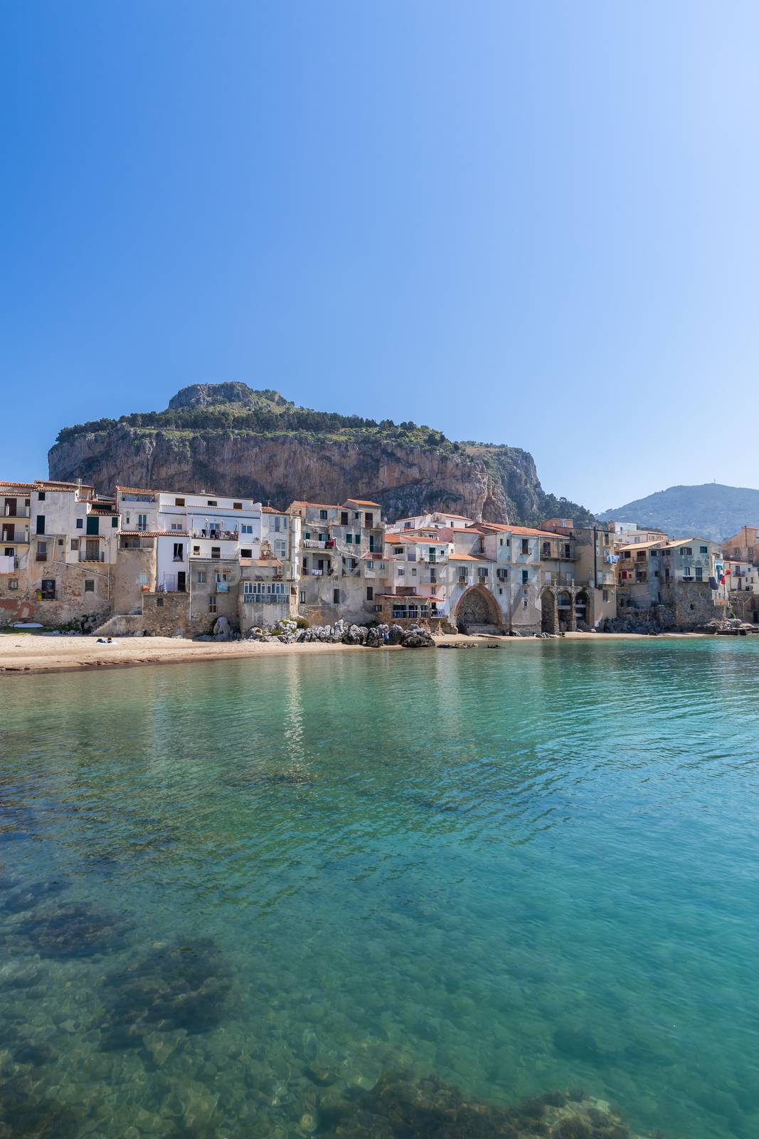 Idyllic view of turquoise sea and houses with Rocca di Cefalu rocky mountain in the background seen from historical old harbour of Cefalu, Sicily, Italy. by tamas_gabor