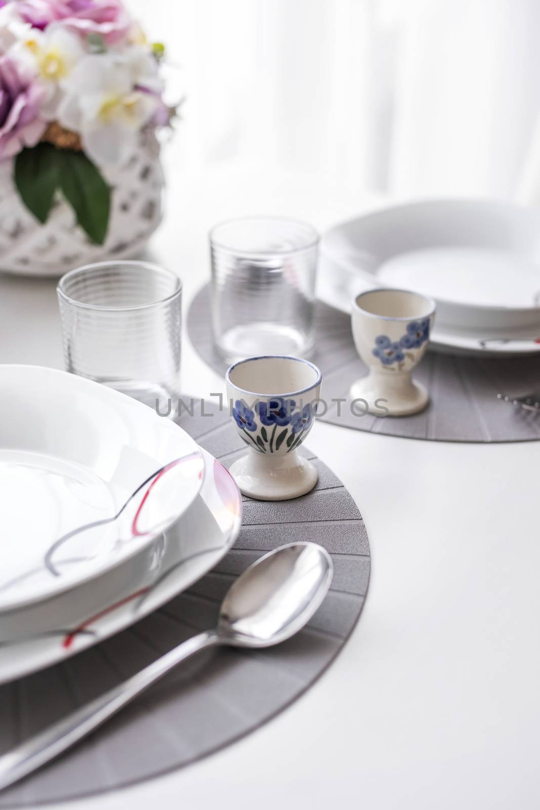 Minimalist white tableware on a white surface dining table in natural light, angled view.