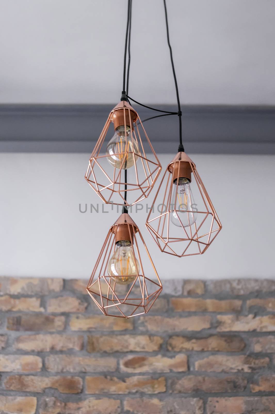 Set of three rose gold light fixtures in front of a white and brick wall background.