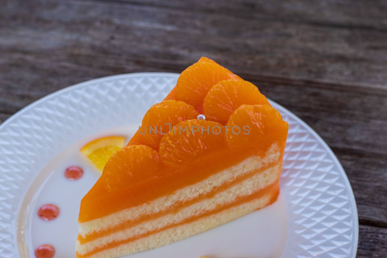 orange cake in a white plate on wooden table by Khankeawsanan