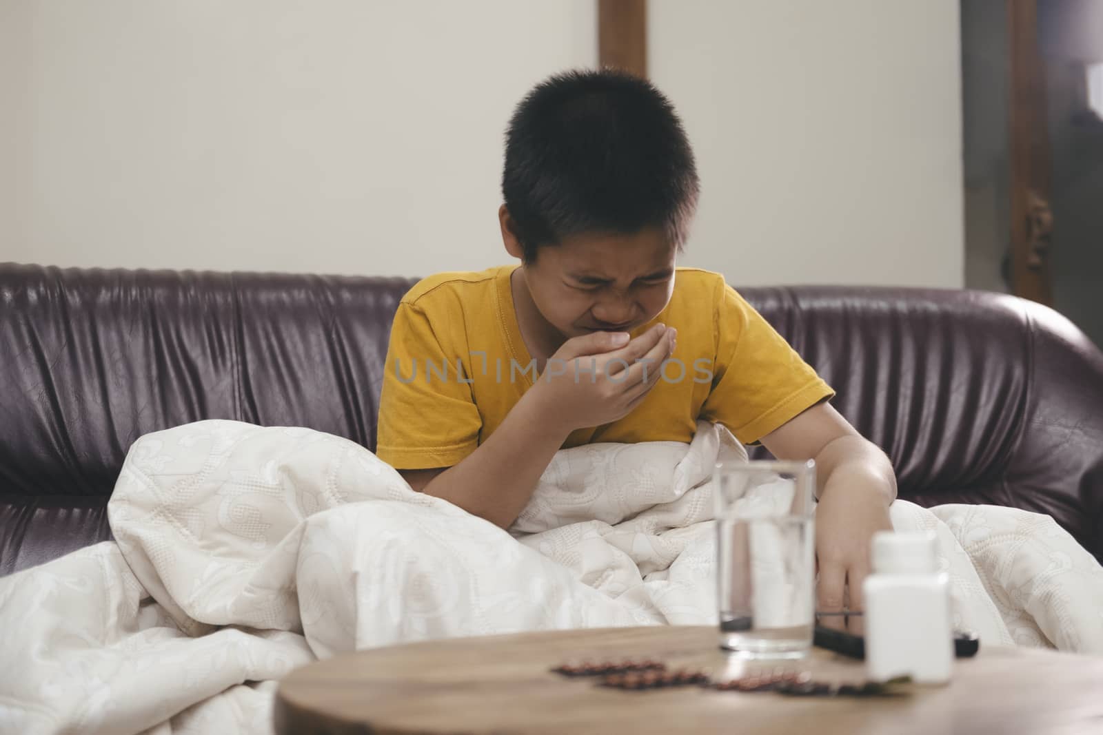 Young ill boy on couch at homes neezing  while at home sick in pajamas, cold and flu healthcare concept