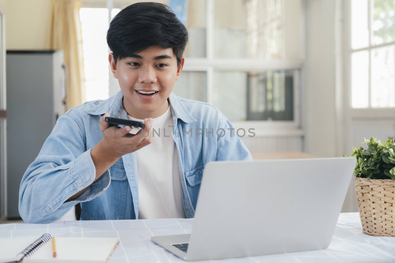 Young man talking on the phone with handfree and using laptop working and meeting online at home. 