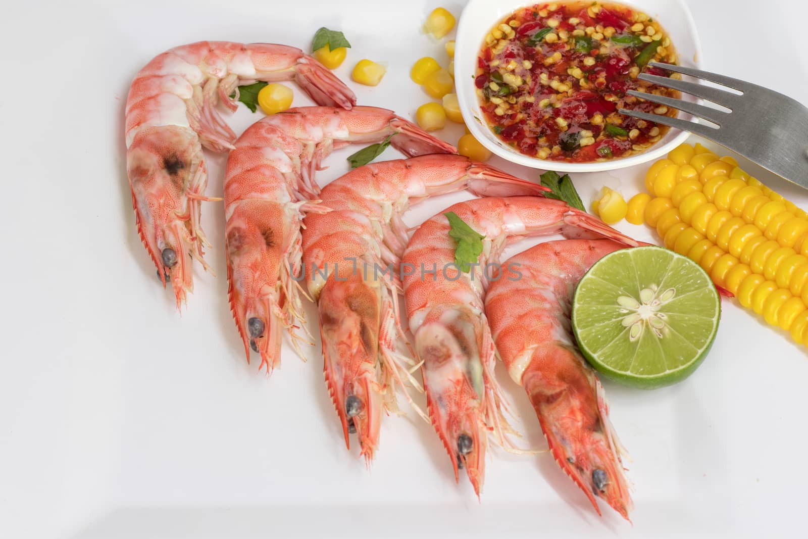 boiled shrimps in white plate with corn, half of lime and spicy seafood dipping sauce