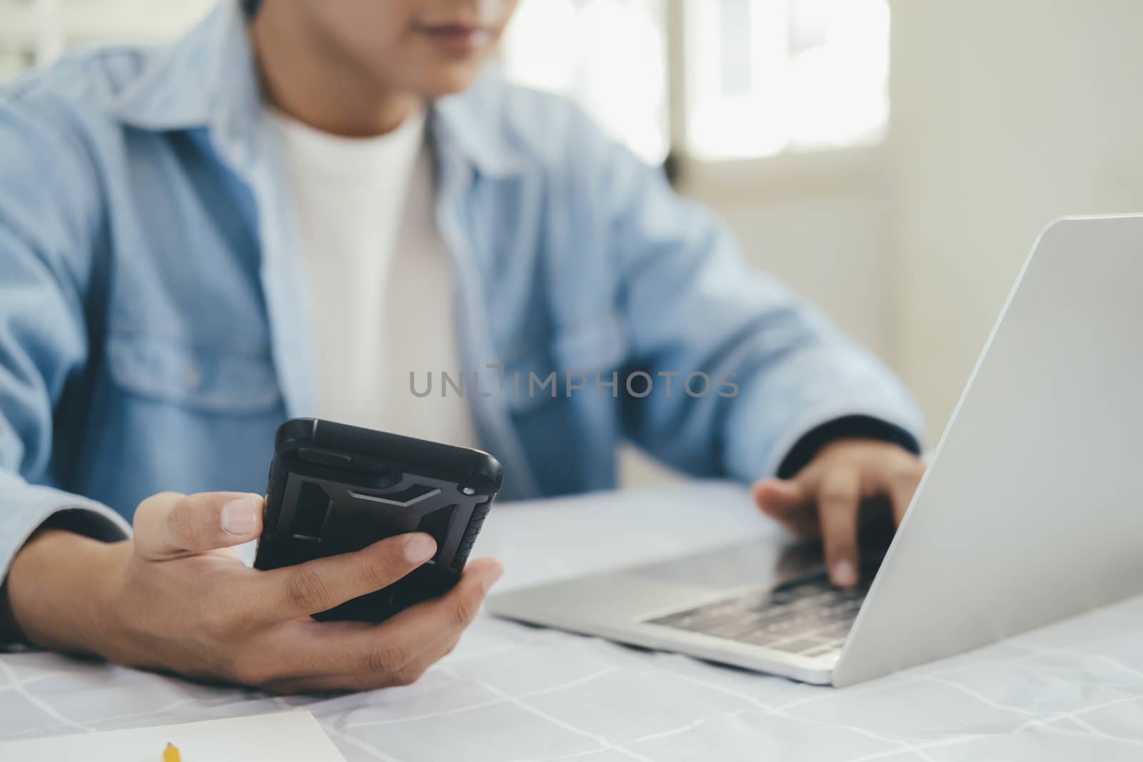 Young man using mobile phone and laptop working online at home or office. Using online connect technology for business, education and communication. 