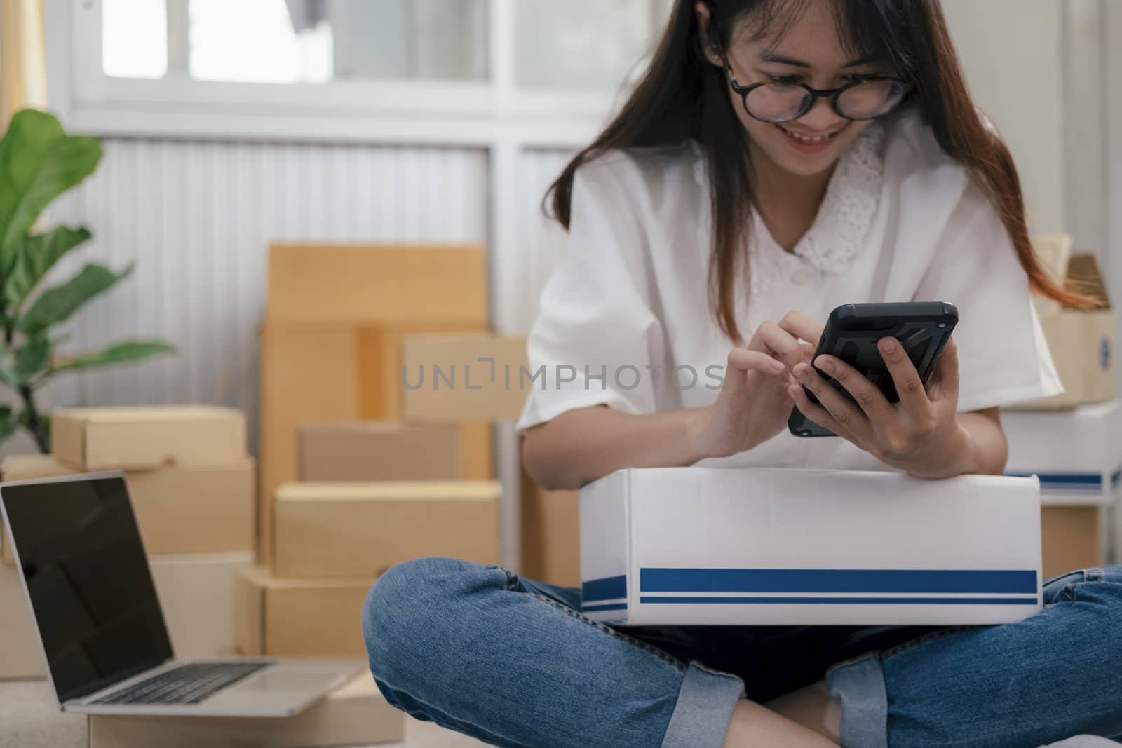 Young entrepreneur working online e-commerce shopping at her shop. Young online seller checking order from customer and prepare parcel box deliver to customers. Online selling and online business e-commerce concept.