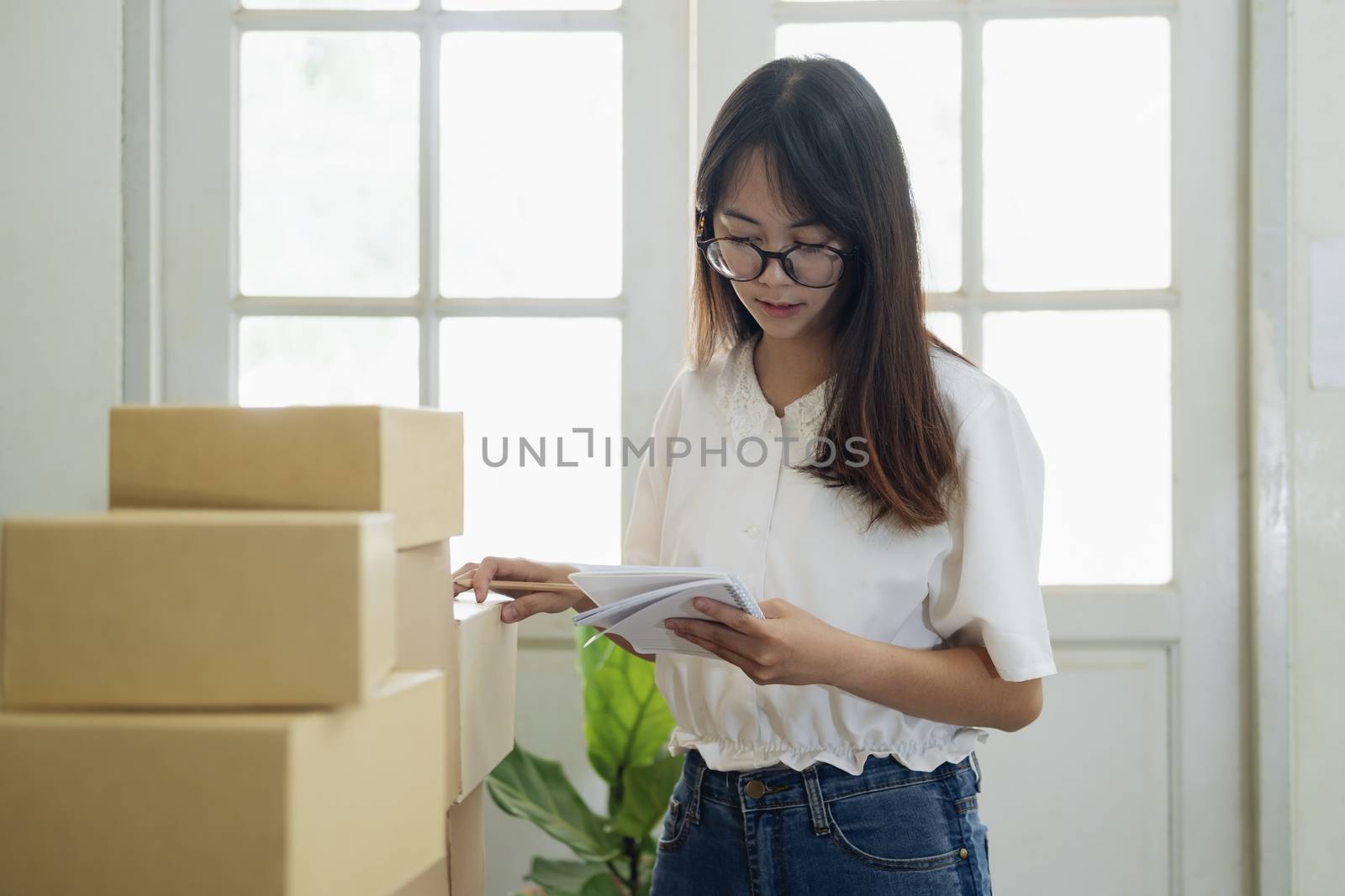Shipping shopping online. Young entrepreneur working online e-commerce shopping at her shop. Young online seller checking order from customer and prepare parcel box deliver to customers. Online selling and online business e-commerce concept.