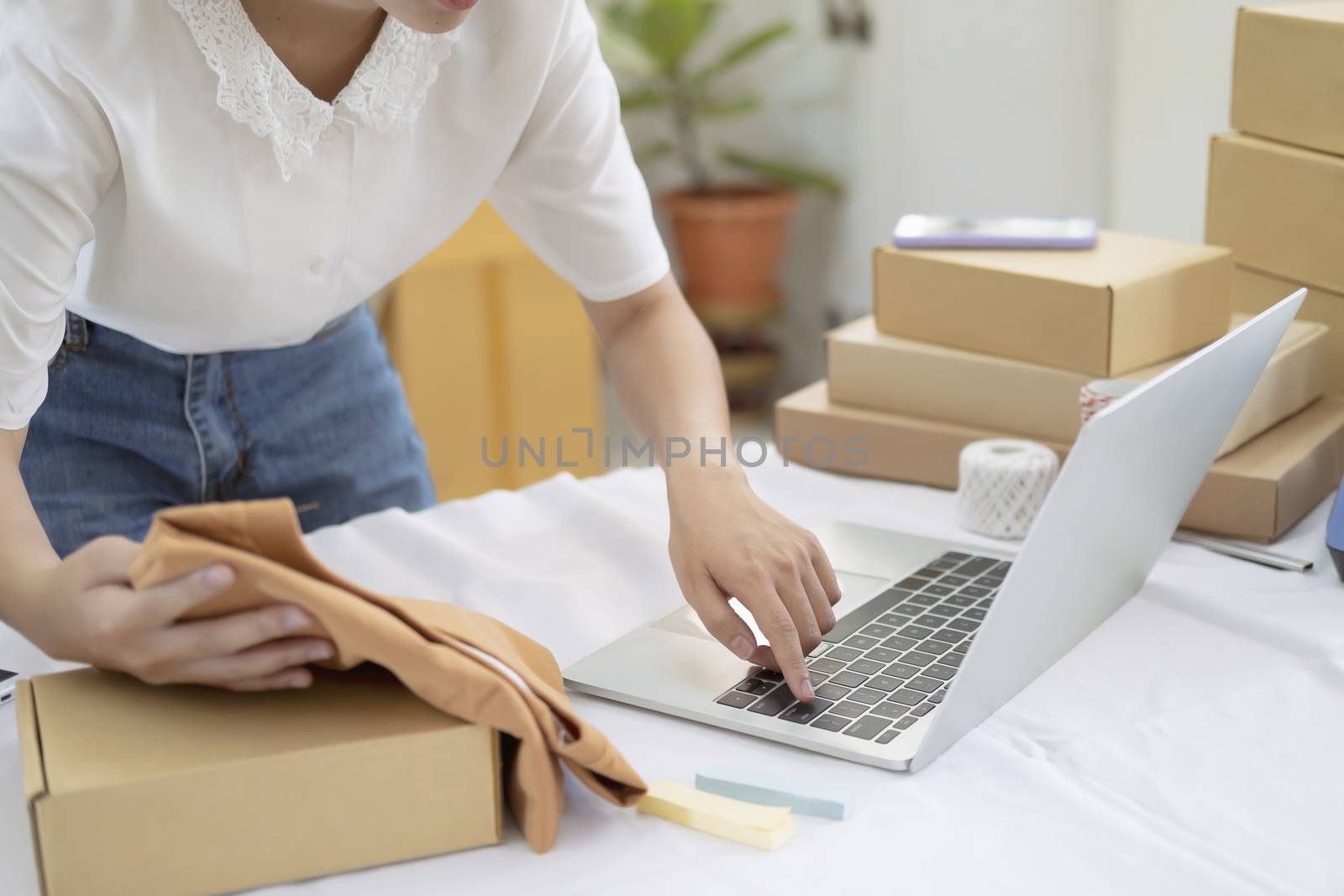 Young entrepreneur working online e-commerce shopping at her shop. Young online seller checking preduct for prepare parcel box deliver to customer. Online selling and online business e-commerce concept.