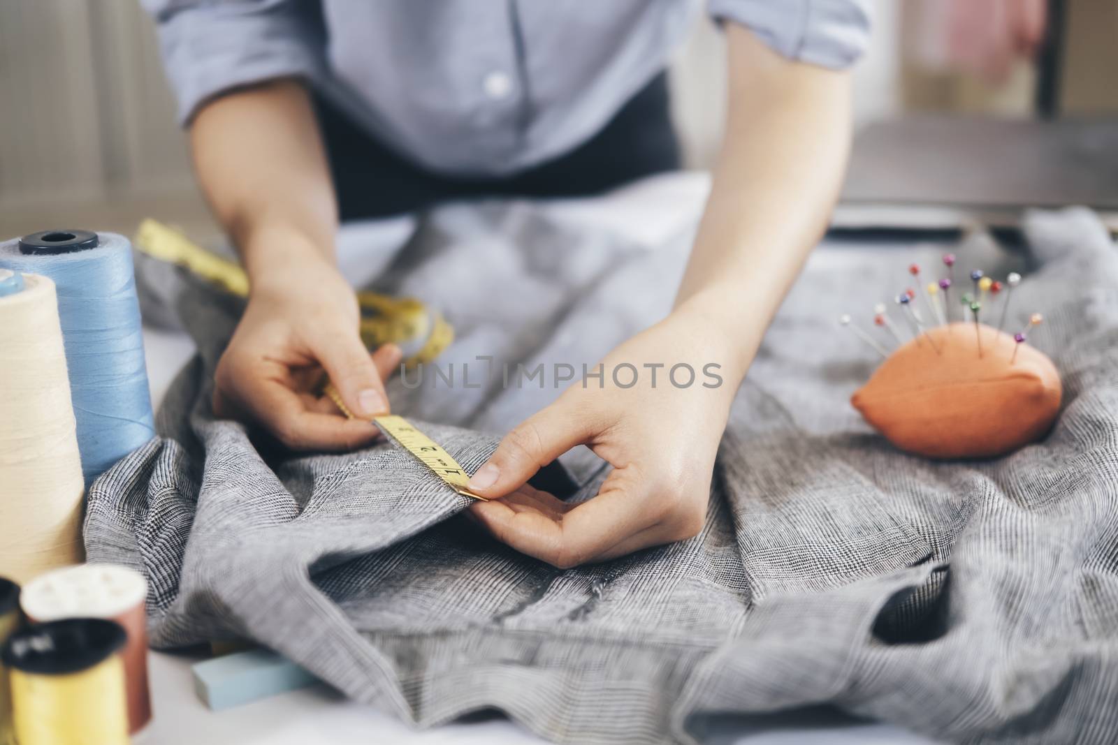 Closeup young woman tailor taking measurements of jacket on on working table.