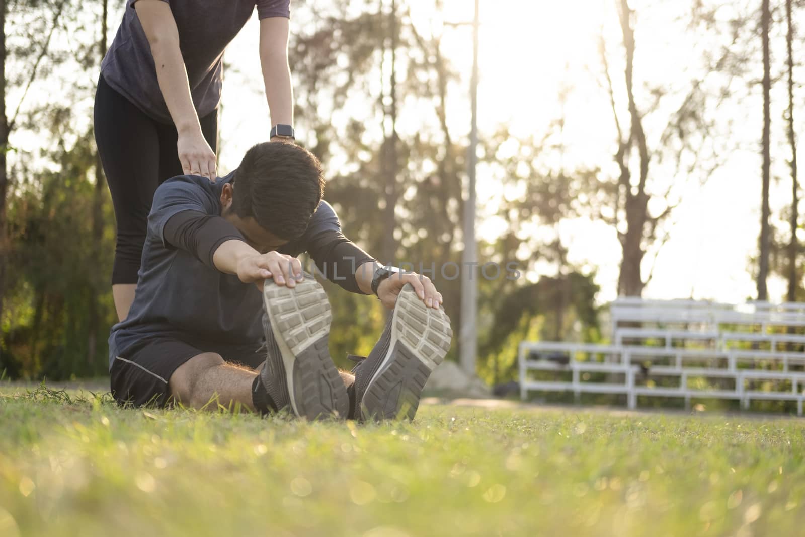 Young man and woman stretching in the park. Young couple cool down after workout exercise.