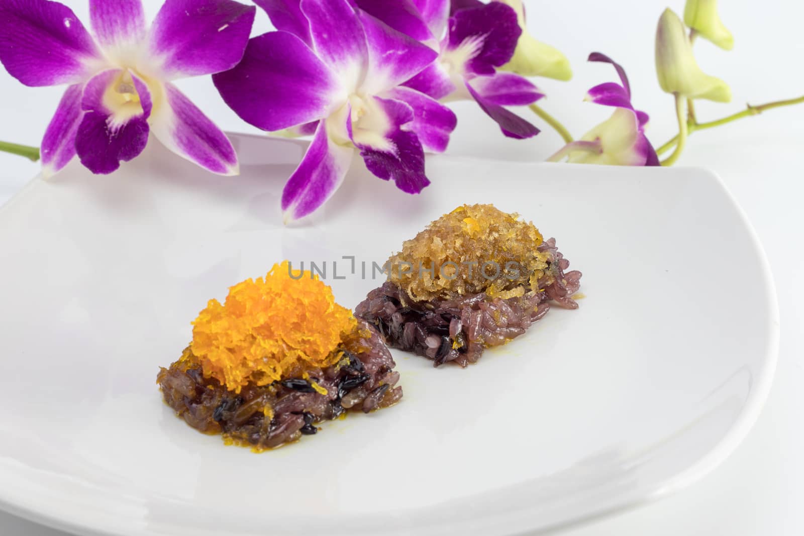 black sweet sticky rice  in white plate decorated with purple orchid