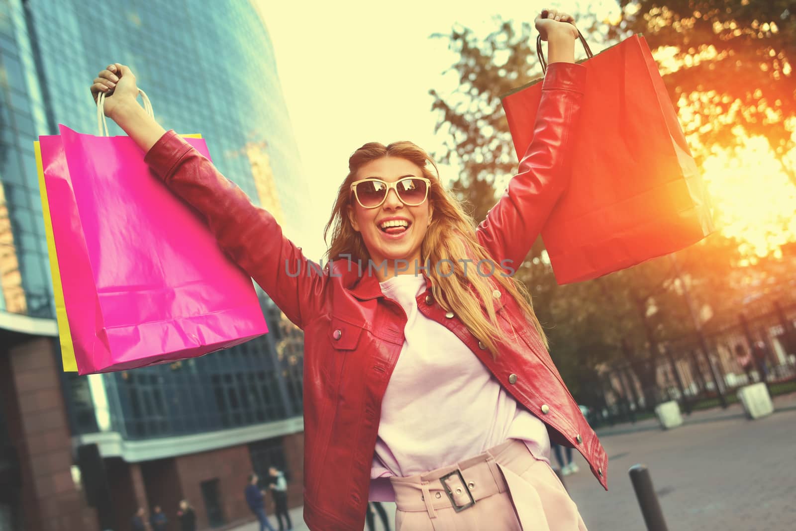 Beautiful smiling girl in sunglasses is holding shopping bags and enjoying her shopping. by Nickstock