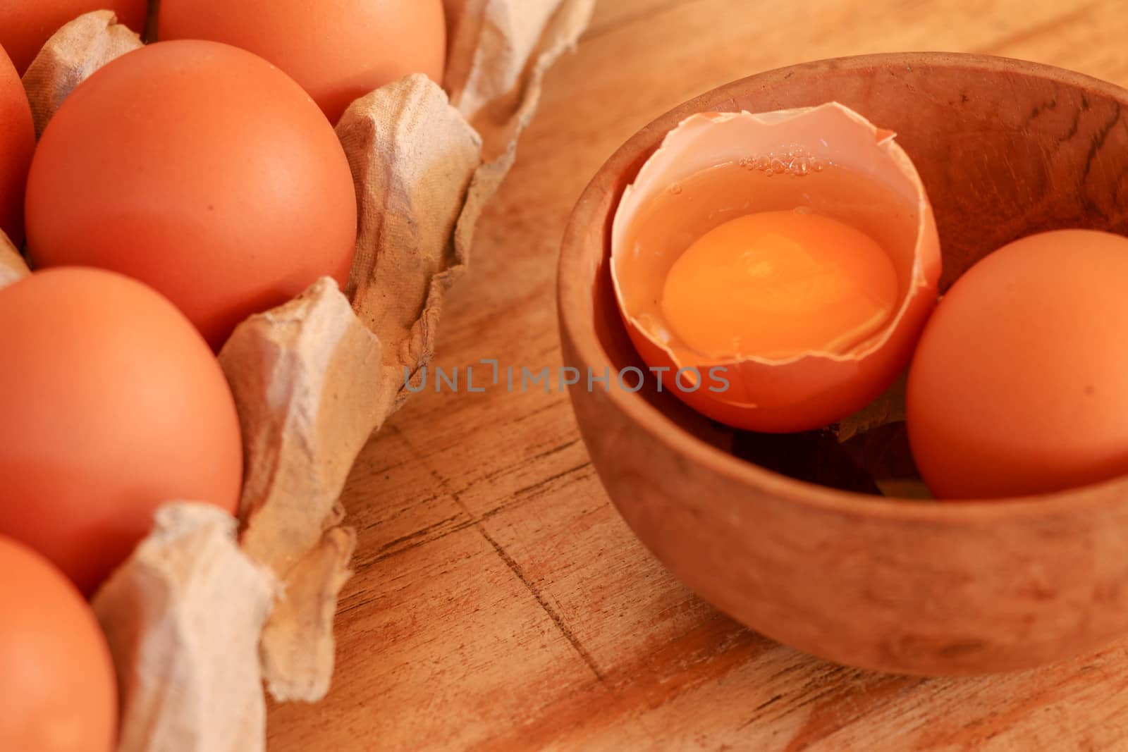 Cracked egg in bowl and egg shells on wooden table.