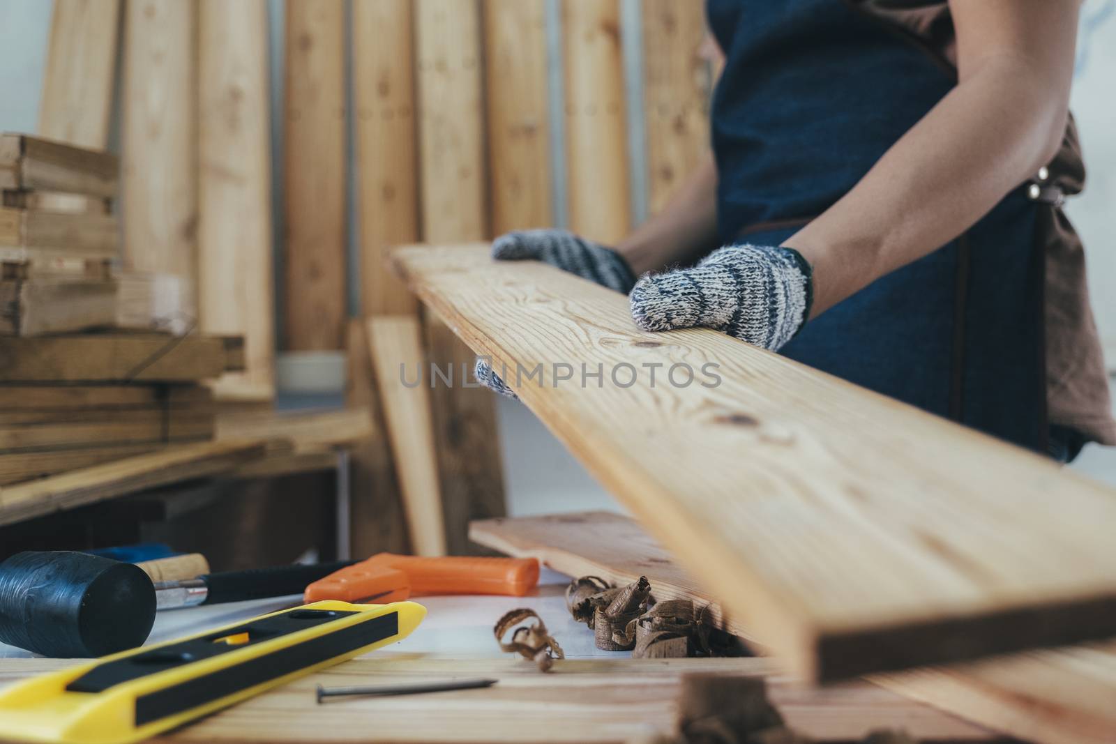 DIY woodworking and furniture making and craftsmanship and handwork concept. Carpenter working on woodworking machines in carpentry shop. Young man working as carpenter and taking wood stock.