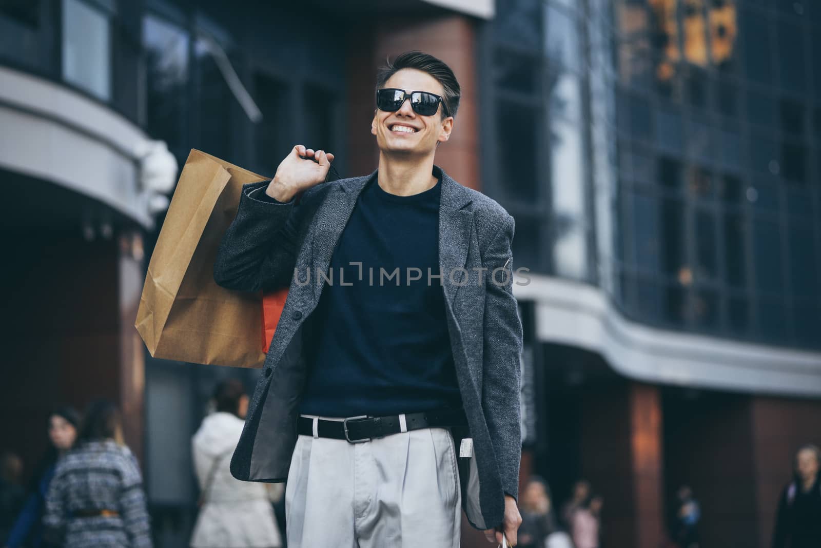 Serious cool guy with sunglasses and paper bags walking at street.